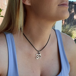 May include: A silver Om pendant necklace with a small purple gemstone on a black cord.