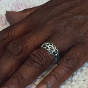 May include: A silver ring with a braided design. The ring is worn on a finger.