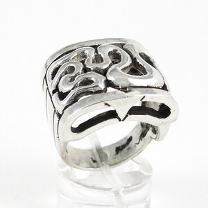 May include: A silver ring with an intricate, abstract design. The ring is wide and has a square shape.