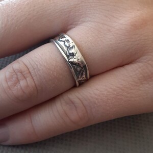 May include: A silver ring with a detailed design of a mountain range.