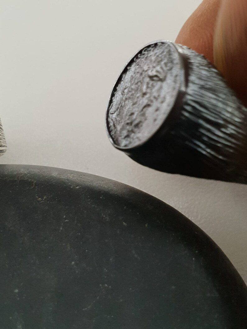 Puede incluir: Un anillo de sello de plata con una superficie texturizada. El anillo se lleva en un dedo.