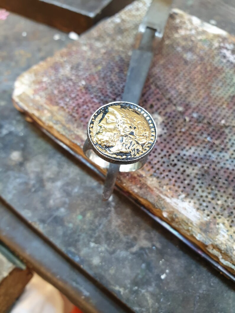 May include: A silver ring with a gold-toned round face featuring a detailed profile of a person's face.