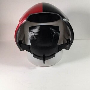 Puede incluir: Un casco negro y rojo con una correa y un interior negro texturizado. El casco est&aacute; sobre una superficie blanca.