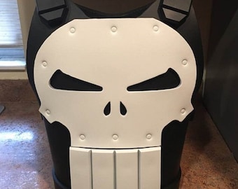 Puede incluir: Una armadura corporal en blanco y negro con un diseño de calavera. La armadura presenta una cara de calavera blanca con cortes de ojos negros y una sección rectangular blanca en la parte inferior. La armadura tiene correas negras para los hombros.
