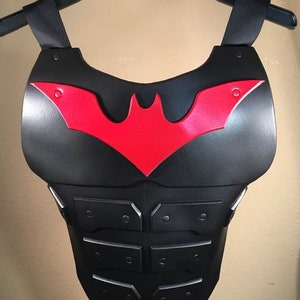 May include: Black and red plastic chest armor with a bat symbol. The chest armor has a textured surface and is designed to look like a superhero costume.