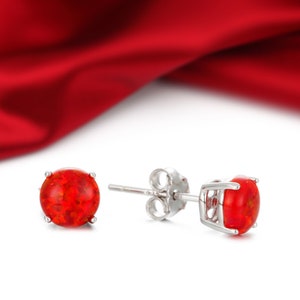 May include: A pair of silver stud earrings with red opal gemstones. The earrings are set against a red satin background.