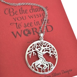 May include: A silver necklace with a tree of life pendant. The pendant is a circle with a detailed tree design. The necklace is on a red background with the text "Be the change you wish to see in the world."