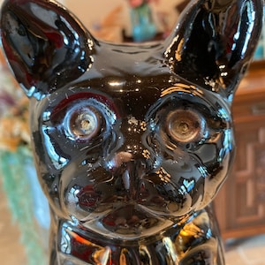 May include: A glossy black ceramic cat figurine with large ears and wide eyes. The cat has a bow tie and a reflective surface. The figurine is a decorative item.