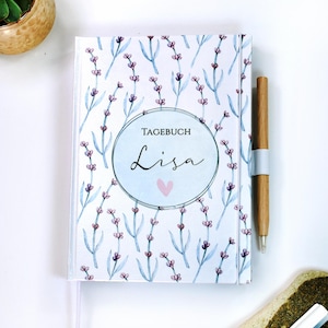 Könnte beinhalten: Ein weißes Tagebuch mit einem Lavendel-Blumenmuster und dem Text "Tagebuch Lisa" in einem Kreis mit einem rosa Herzen.