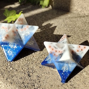 May include: Two blue and white star-shaped resin ornaments with copper accents. The ornaments are made with a variety of materials, including glitter and mica.