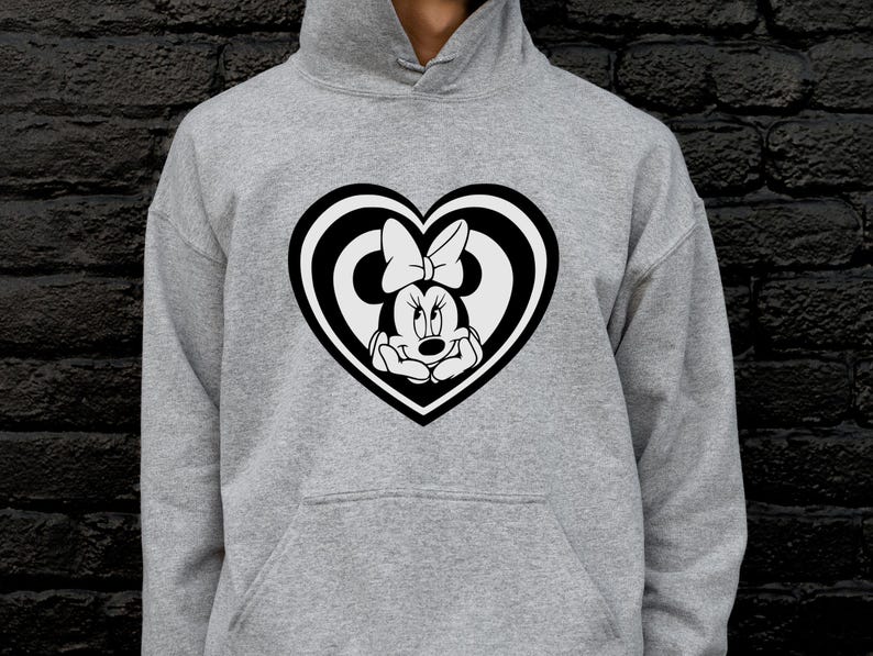 May include: A gray hoodie featuring a black and white Minnie Mouse design inside a heart shape. The Minnie Mouse graphic includes her face and bow. The hoodie has a front pocket and a hood.
