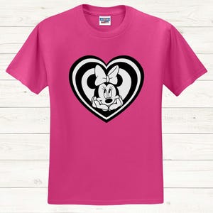 May include: A magenta t-shirt featuring a black and white Minnie Mouse graphic inside a heart shape. The graphic shows Minnie Mouse with her hands under her chin. The t-shirt is made of a soft material.