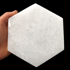 May include: A white hexagonal selenite charging plate. The plate is smooth and polished, with a slightly cloudy appearance.