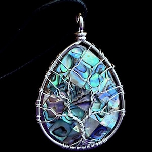 May include: A teardrop-shaped pendant featuring a mosaic of iridescent abalone shell pieces in shades of blue, green, and purple. The shell is encased in a silver-toned wire frame with a wire-wrapped tree design overlay and a black cord.