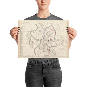 May include: A vintage map of Ancient Rome, printed on a cream-colored paper with brown and pink details. The map shows the city's layout with rivers, roads, and buildings. The title "Plan of Ancient Rome" is printed at the bottom.