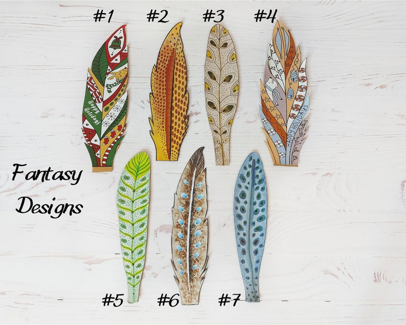May include: Seven decorative feather designs with various patterns and colours. The feathers include green, red, yellow, brown, and blue hues. Some feathers have the text "Happy Holidays". The words "Fantasy Designs" are also visible in the image.