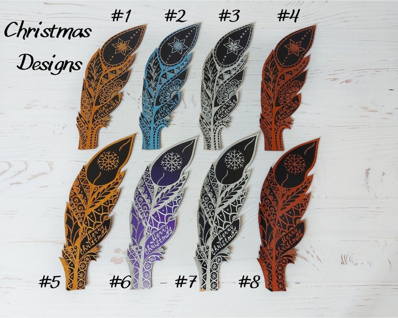 Puede incluir: Ocho adornos decorativos con forma de pluma en tonos dorados, azules, plateados y naranjas. Cada pluma presenta dise&ntilde;os sim&eacute;tricos y detallados, con la inscripci&oacute;n "Merry Christmas". Tambi&eacute;n se ve el texto "Christmas Designs".