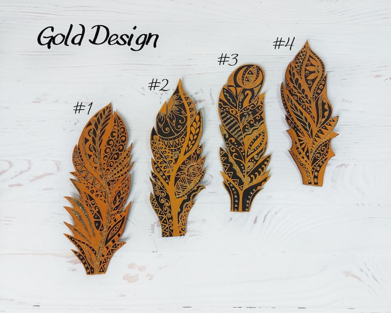 Puede incluir: Cuatro recortes decorativos de plumas con intrincados dise&ntilde;os en negro y dorado. Las plumas est&aacute;n numeradas y etiquetadas como "Gold Design". Cada pluma tiene un patr&oacute;n &uacute;nico, con elementos geom&eacute;tricos y florales.