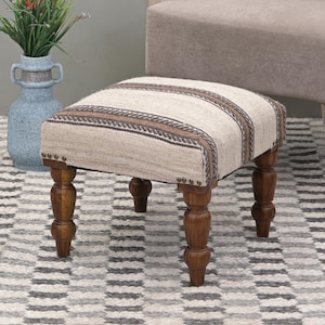 Puede incluir: Un pequeño otomano rectangular con una parte superior de tela a rayas y patas de madera torneadas. El otomano está sobre una alfombra estampada.