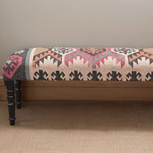 K&ouml;nnte beinhalten: Rechteckige gepolsterte Bank mit gemusterter Stoffoberfl&auml;che. Der Stoff weist ein geometrisches Design in Beige, Rot, Orange und Schwarz auf. Sie hat vier schwarze, gedrechselte Beine. Geeignet f&uuml;r Flur oder Wohnzimmer.