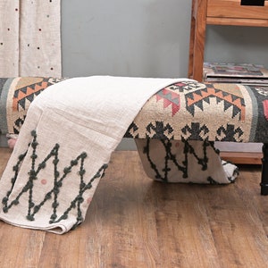 K&ouml;nnte beinhalten: Dekorative Bank mit gemustertem Sitz in Beige-, Schwarz-, Rot- und Oranget&ouml;nen. Die Bank hat schwarze, gedrechselte Beine und ist mit einer cremefarbenen Decke mit dunkelgr&uuml;nen und rosa Akzenten drapiert. Wohnkultur.