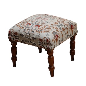 May include: A small, upholstered footstool with a rectangular top and four turned wooden legs. The fabric features a repeating pattern in shades of red, brown, gray, and cream. The legs are a dark, polished wood.