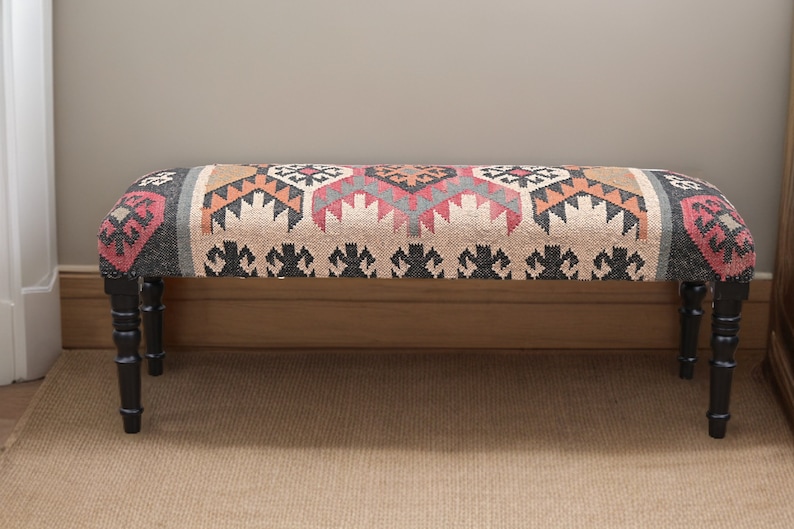 K&ouml;nnte beinhalten: Rechteckige gepolsterte Bank mit gemusterter Stoffoberfl&auml;che. Der Stoff weist ein geometrisches Design in Beige, Rot, Orange und Schwarz auf. Sie hat vier schwarze, gedrechselte Beine. Geeignet f&uuml;r Flur oder Wohnzimmer.