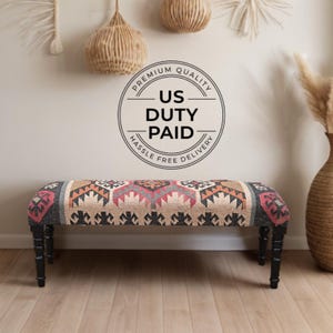 K&ouml;nnte beinhalten: Gepolsterte Bank mit geometrischem Muster in Rot-, Orange- und Graut&ouml;nen. Die Bank hat schwarze Beine und eine rechteckige Form. Der Text "US Duty Paid" befindet sich in einem Kreis &uuml;ber der Bank.