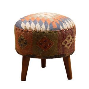 Può includere: Un pouf rotondo imbottito con un colorato motivo geometrico in arancione, blu e crema. I lati presentano un design patchwork con varie forme di rombi. Il pouf ha tre gambe in legno e misura circa 38 cm di diametro.