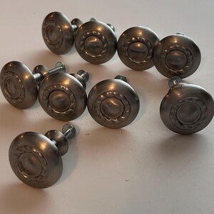 May include: Nine silver cabinet knobs with a decorative design. The knobs have a round shape and a raised center with a circular pattern.