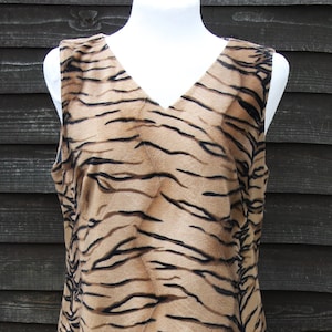 K&ouml;nnte beinhalten: Ein &auml;rmelloses Kleid mit Tigermuster. Das Kleid ist aus weichem, pl&uuml;schigem Stoff und hat einen V-Ausschnitt.