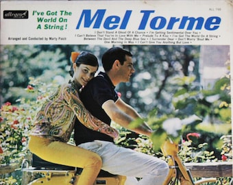Pode incluir: Uma capa de álbum de vinil vintage com um homem e uma mulher a andar de mota amarela. O título do álbum é "I've Got The World On A String!" de Mel Torme. A capa do álbum é ambientada num fundo de folhagem verde e flores.