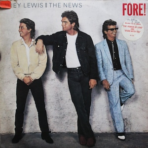 Puede incluir: Una portada de álbum de vinilo vintage con una banda llamada "Jey Lewis and The News". El título del álbum es "FORE!" y la portada presenta a tres hombres con ropa informal de pie contra una pared blanca.
