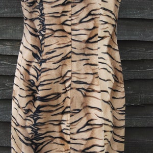 K&ouml;nnte beinhalten: Ein &auml;rmelloses Kleid mit Tigermuster. Das Kleid ist braun und schwarz mit einem Rei&szlig;verschluss auf der R&uuml;ckseite.
