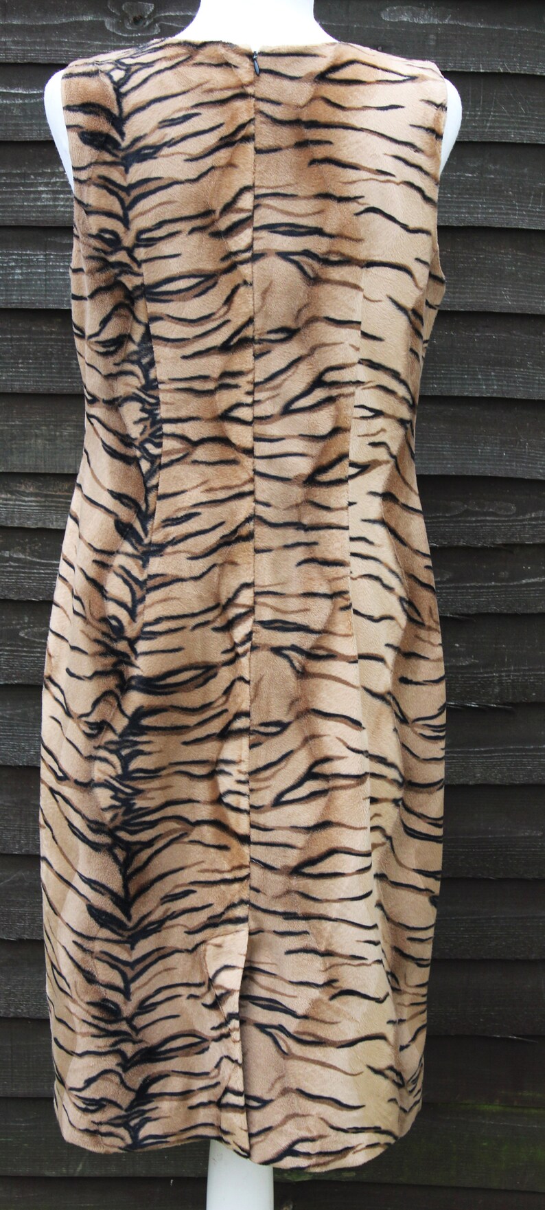 K&ouml;nnte beinhalten: Ein &auml;rmelloses Kleid mit Tigermuster. Das Kleid ist braun und schwarz mit einem Rei&szlig;verschluss auf der R&uuml;ckseite.