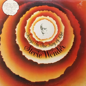 Op de afbeelding: Albumhoes voor Stevie Wonder's "Songs in the Key of Life". Het ontwerp toont concentrische oranje en bruine cirkels met een portret van Stevie Wonder in het midden. De albumtitel en artiestennaam staan in elegant schrift.