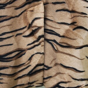 K&ouml;nnte beinhalten: Nahaufnahme eines braunen und schwarzen Stoffes mit Tigermuster. Der Stoff hat eine weiche, flauschige Textur.