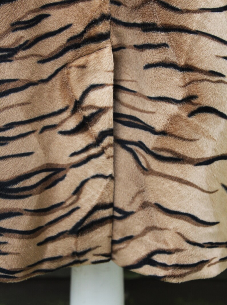 K&ouml;nnte beinhalten: Nahaufnahme eines braunen und schwarzen Stoffes mit Tigermuster. Der Stoff hat eine weiche, flauschige Textur.
