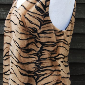 K&ouml;nnte beinhalten: Ein &auml;rmelloses Kleid mit Tigermuster. Das Kleid ist aus weichem, pl&uuml;schem Stoff und hat einen V-Ausschnitt.