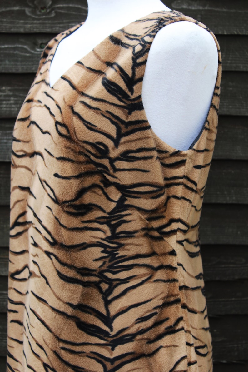 K&ouml;nnte beinhalten: Ein &auml;rmelloses Kleid mit Tigermuster. Das Kleid ist aus weichem, pl&uuml;schem Stoff und hat einen V-Ausschnitt.