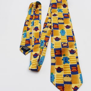 Puede incluir: Una corbata de seda amarilla con un patrón repetido de personajes azules de Mr. Men, teteras y tazas. Los personajes son Mr. Grumpy, Mr. Tickle y Mr. Messy.