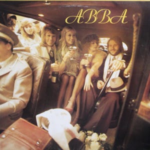 Puede incluir: Portada del álbum del grupo ABBA. La imagen muestra a los miembros de la banda dentro de un coche, con copas de champán y una botella. Los miembros de la banda visten atuendos de los años 70. El título del álbum "ABBA" está en escritura dorada.