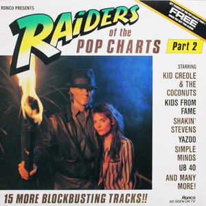 Peut inclure: Pochette d'album pour "Raiders of the Pop Charts Part 2" avec un homme et une femme, et une torche. La couverture comprend le texte "15 More Blockbusting Tracks!!" et répertorie des artistes tels que Kid Creole & The Coconuts.