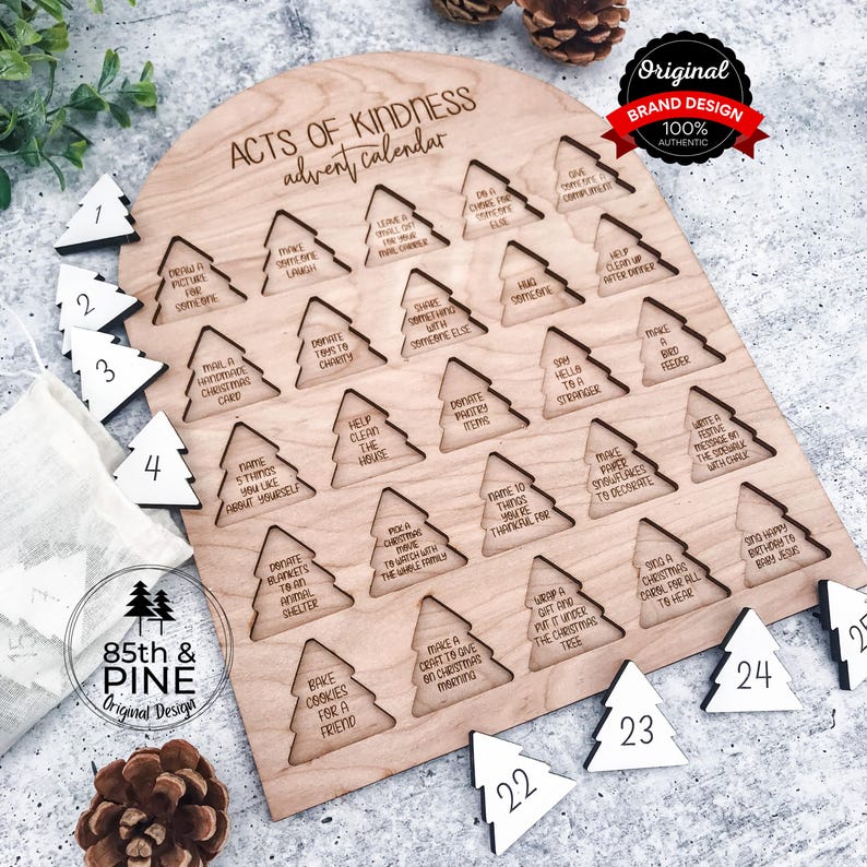 May include: A wooden Acts of Kindness advent calendar with a light wood finish. The calendar features 25 tree-shaped cutouts with daily acts of kindness. Includes numbered white wooden tree ornaments. The top reads "Acts of Kindness advent calendar."
