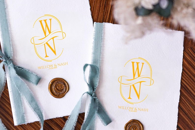 Puede incluir: Dos tarjetas blancas con un monograma dorado de las letras "W" y "N" est&aacute;n atadas con cintas azul claro. Las tarjetas tienen un sello de cera dorado con un dise&ntilde;o de coraz&oacute;n. El texto "WILLOW & NASH" est&aacute; impreso en las tarjetas.