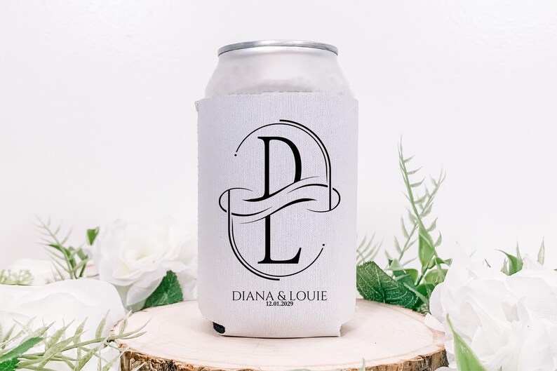Puede incluir: Un enfriador de latas blanco con un dise&ntilde;o de monograma negro con las letras "D" y "L" entrelazadas. Los nombres "DIANA & LOUIE" y la fecha "12.01.2029" est&aacute;n impresos debajo. El enfriador est&aacute; sobre una superficie de madera.