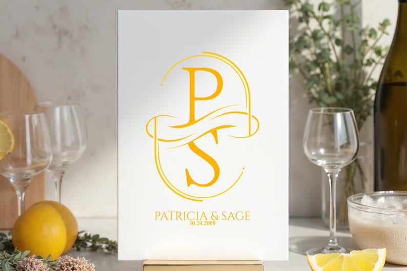 Puede incluir: Un letrero blanco con un monograma dorado de las letras "P" y "S" entrelazadas, con los nombres "Patricia & Sage" y la fecha "10.24.2009" debajo. El letrero se muestra sobre un soporte dorado.