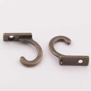 May include: Two antique bronze hooks with a simple design. Each hook has a rectangular base with a single hole and a curved hook.