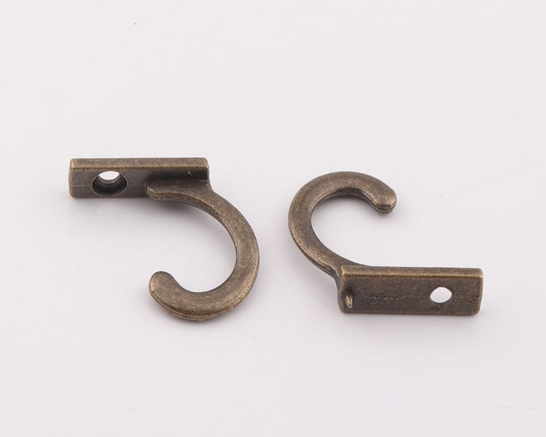 May include: Two antique bronze hooks with a simple design. Each hook has a rectangular base with a single hole and a curved hook.