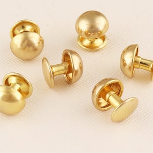 May include: Six gold-toned metal dome-shaped studs with a flat back. The studs have a smooth, shiny finish.